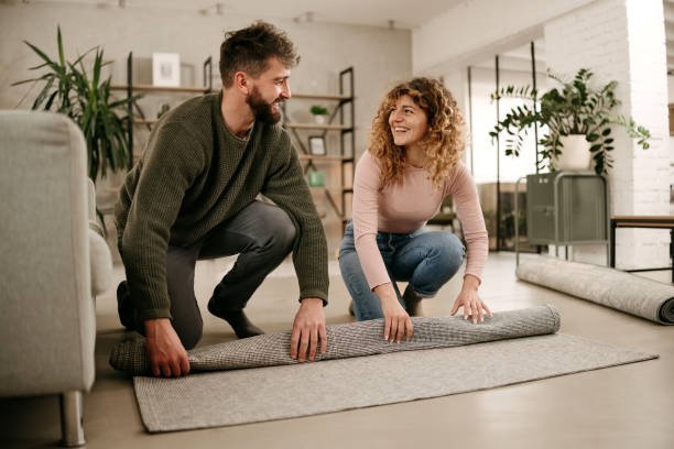Man and a woman roll a carpet in an apartment